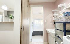 リフォーム後のお風呂と洗面脱衣所　ピンクの壁紙と白い棚と洗面化粧台が優しい色合いの空間に